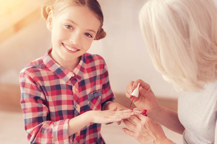 Mindful grandmother painting nails of her stylish granddaughter