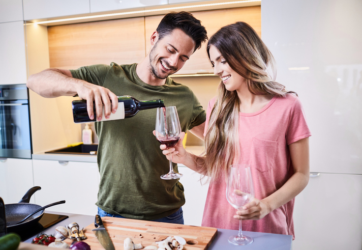 Young man pouring a glass of wine for his girlfriend in the kitchen, celebrating together