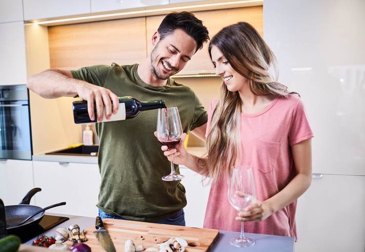 Young man pouring a glass of wine for his girlfriend in the kitchen, celebrating together